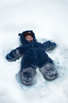 a baby is laying in the snow wearing a blue jacket and hat with his eyes closed