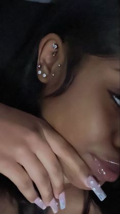 a close up of a person with piercings on her ear and hand over their face