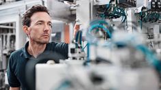 a man standing in front of a machine with wires on the side and other machines behind him