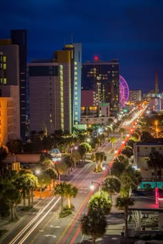 a city street at night with tall buildings and palm trees in the foreground, lit up by bright lights