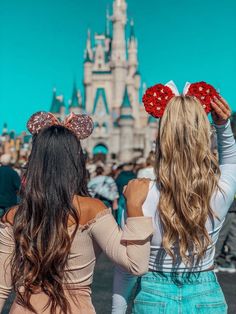 two girls in front of a castle with minnie mouse ears on their heads, looking at the sky