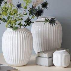 two white vases sitting on top of a table next to a silver container with flowers in it