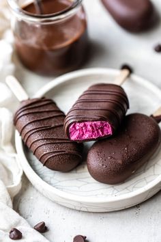 two pieces of chocolate covered ice cream on a white plate with pink candy in the middle