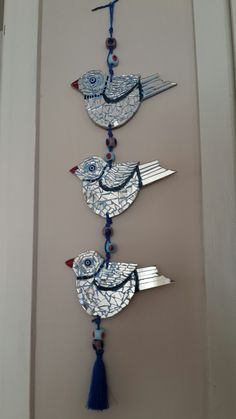 three blue birds hanging from a wall with tassels on it's sides