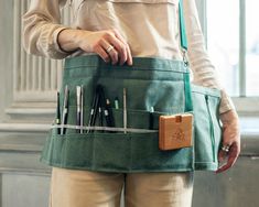 a woman holding a green apron with tools in it's pocket and an object hanging from the back