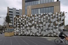 a man riding a bike past a building with geometric design on the front and side