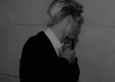 a man adjusting his tie while standing in front of a wall with white tiles on it