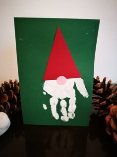 a handprinted christmas card with an image of a gnome on it and pine cones in the background