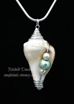 a white shell with two green pearls on a silver chain hanging from a black background