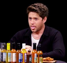 a man sitting at a table with many bottles of sauces on the table in front of him