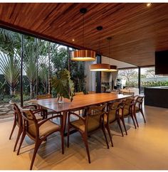 a large wooden table surrounded by chairs in a room with glass walls and floor to ceiling windows