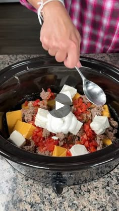 a person spooning food out of a crock pot with cheese and tomatoes on top