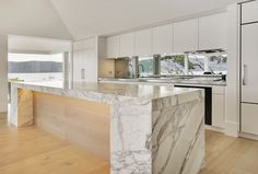 a large kitchen with marble counter tops and white cabinetry, along with hardwood floors