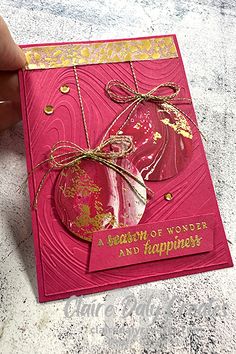 a hand holding a pink and gold christmas ornament on top of a card