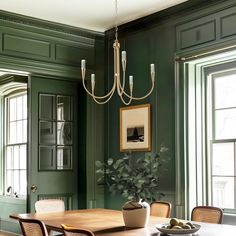 a dining room with green walls and wooden table surrounded by chairs, potted plants and framed pictures on the wall