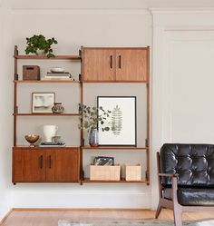 a black leather chair sitting in front of a wooden shelf filled with books and plants