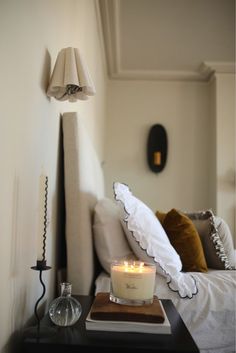 a lit candle sits on top of a table in front of a bed with white sheets and pillows