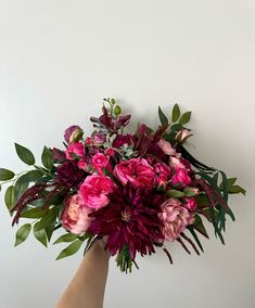 a hand holding a bouquet of flowers against a white wall with green leaves on it