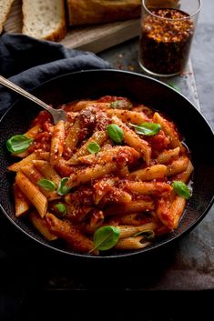 a bowl filled with pasta and sauce on top of a table next to bread slices