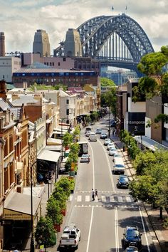 a city street with cars parked on both sides and a bridge in the background