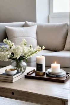 a coffee table with candles, flowers and books on it in front of a couch