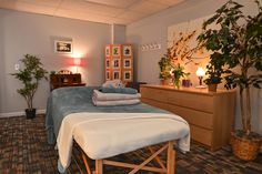 a massage room with towels and plants on the bed in front of a dresser next to a potted plant