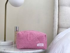 a pink towel sitting on top of a white table next to a lamp and bed