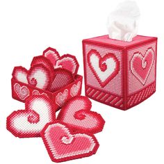 the tissue box has hearts on it and is next to two rolls of toilet paper