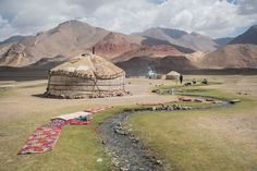 a small hut in the middle of nowhere with mountains in the background and people sitting outside