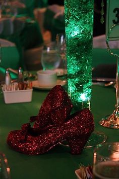 a green table topped with lots of silverware next to a tall vase filled with red glitter shoes