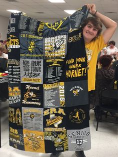 a young man holding up a quilt made from t - shirts in an office setting