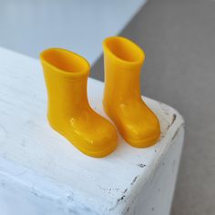 two yellow rubber boots sitting on top of a white piece of wood next to each other