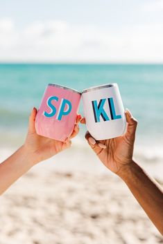 two people holding up pink and blue cans with the words spk on them in front of an ocean