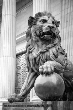 a statue of a lion holding a ball in front of some pillars with columns behind it