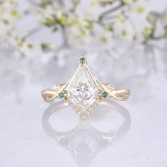 an engagement ring with a princess cut diamond surrounded by green and white diamonds on a reflective surface