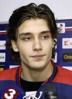 a young man in a red and blue jersey is talking into a microphone while wearing a black t - shirt