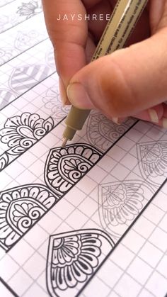 someone is holding a pencil and drawing on paper with an intricate pattern in the background