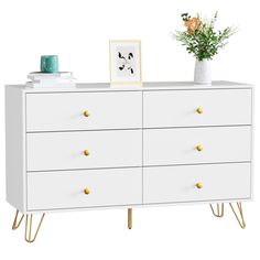 a white dresser with gold legs and a plant on top, against a white background