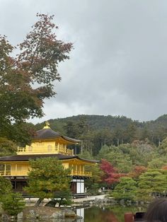 a yellow building sitting on top of a lush green hillside next to a lake and forest