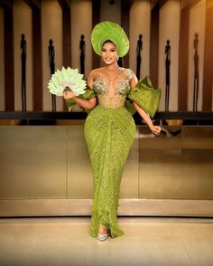 a woman in a green dress and headdress holding two large flower bouquets