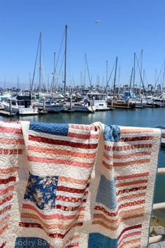 an american flag quilt hanging on a clothesline in front of a marina filled with boats