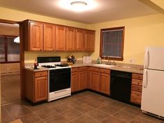 an empty kitchen with white appliances and wood cabinets in the corner, along with brown tile flooring