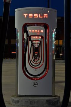 an electric car charging station at night with its lights on and the word tesla spelled in red