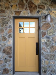 a yellow front door on a stone building with a light hanging from it's side