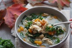 a person holding a spoon in a bowl of chicken and kale soup on a table