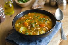 a black bowl filled with soup on top of a wooden cutting board next to a spoon