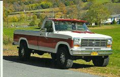 a red and white truck parked on the side of a road next to a lush green hillside