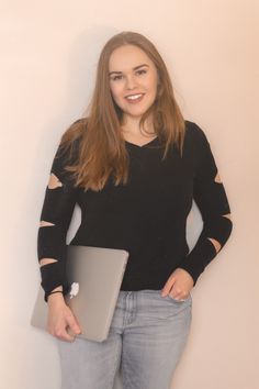 a young woman holding a laptop computer in her right hand and smiling at the camera