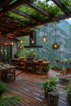 an outdoor kitchen and dining area on a deck overlooking a lake with mountains in the background