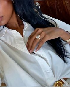 a woman with long black hair wearing a white shirt and gold rings on her finger